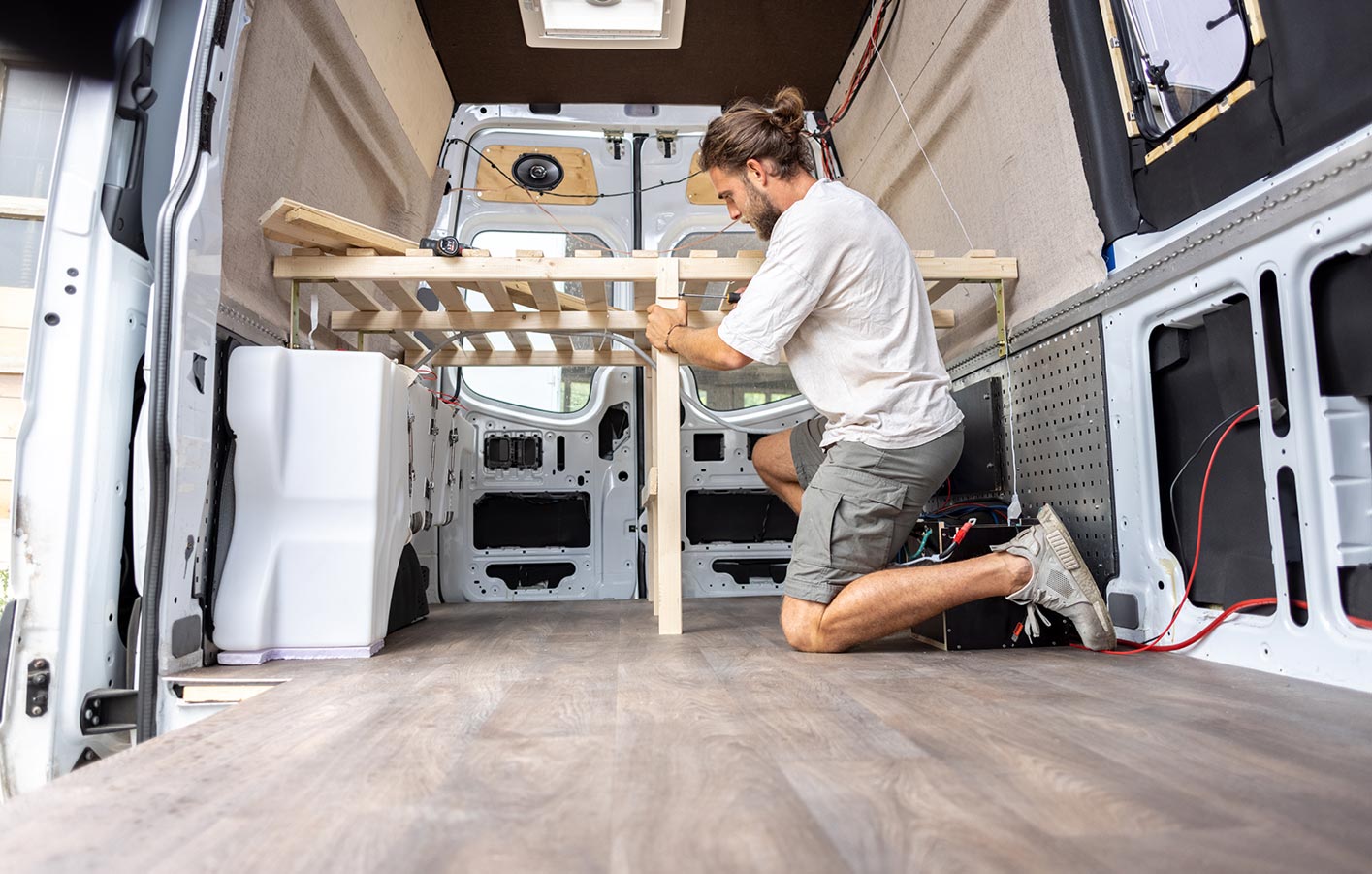 DIY-Wohnmobil: Praktischer Innenausbau mit nachhaltigem Holz Ein Mann baut ein Bettuntergestell in einem Wohnmobil aus nachhaltigen Holzmaterialien, zeigt den praktischen DIY-Ausbauprozess.