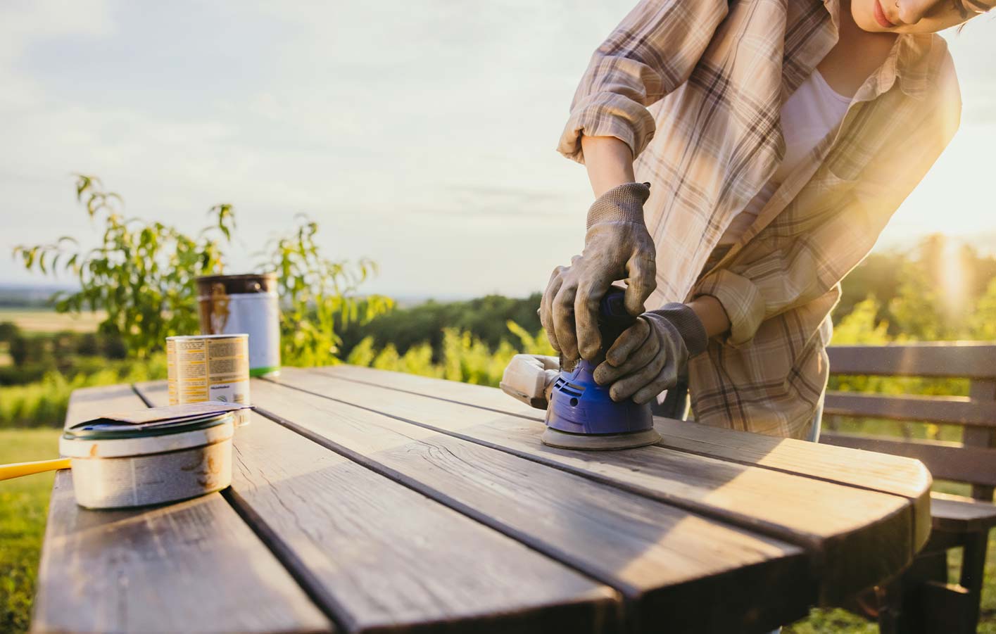 Gartenmöbel aus Holz renovieren - erst abschleifen und dann streichen Frau schleift Gartentisch aus Holz ab