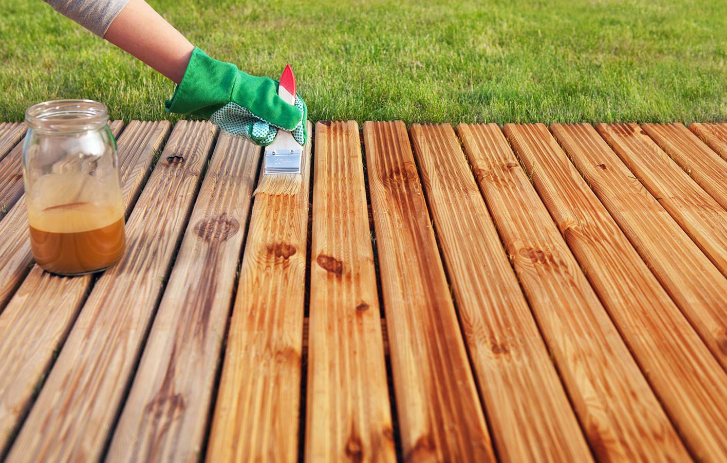 Terrassendielen aus Holz streichen - Holzschutz für die Terrasse Frau streicht Terrassendielen aus Holz